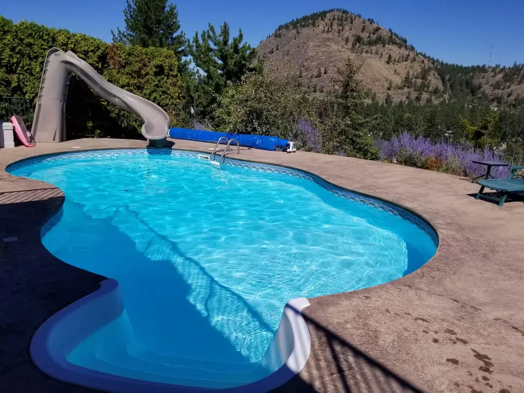 Swimming pool with curved water slide and hillside backdrop