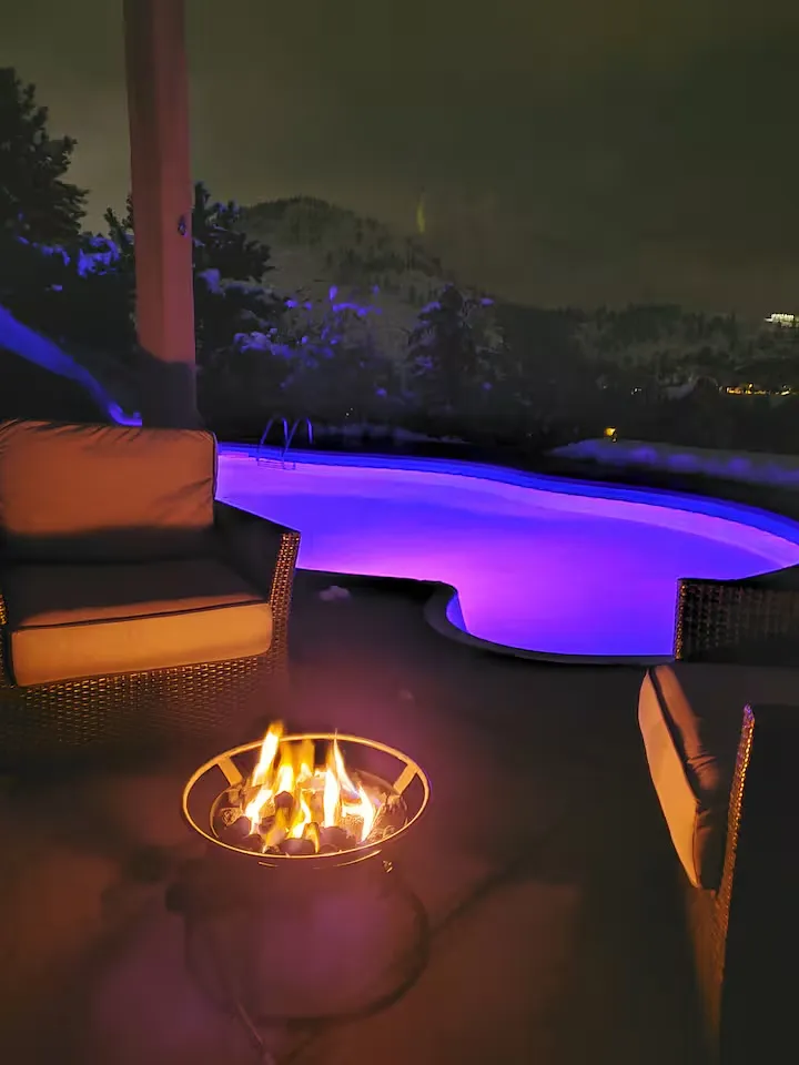 Pool lit purple at dusk beside a flame table